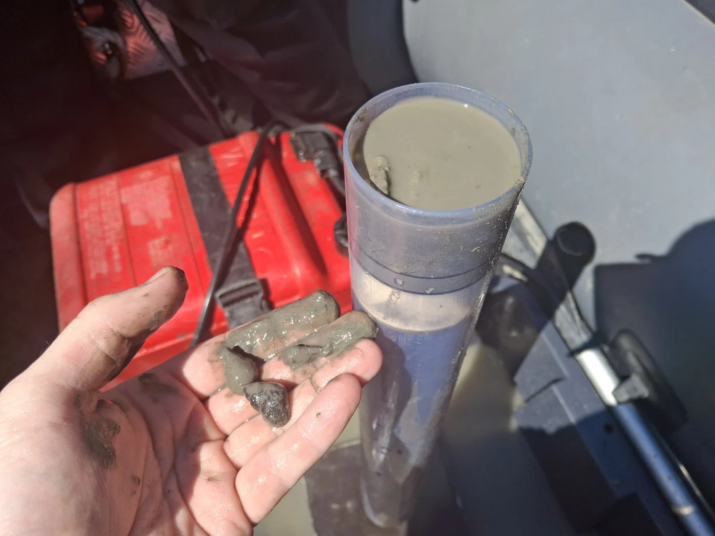 Hand holding a sediment sample beside field equipment